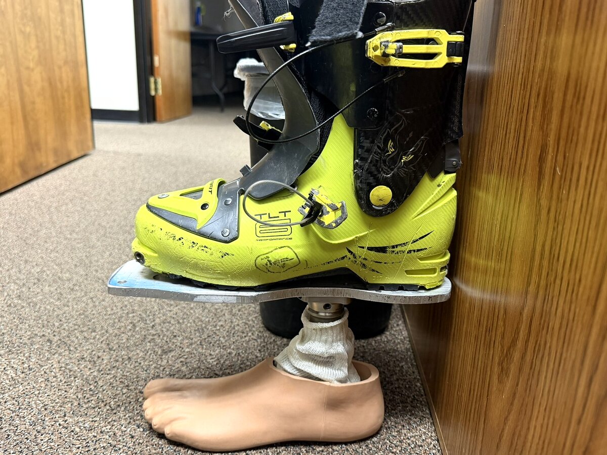 Ski boot mounted on prosthetic ankle mechanism next to a cosmetic foot